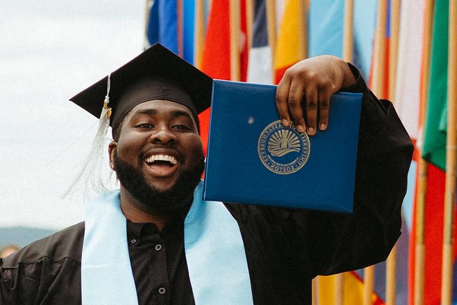 student wearing graduation cap holds diploma in hand